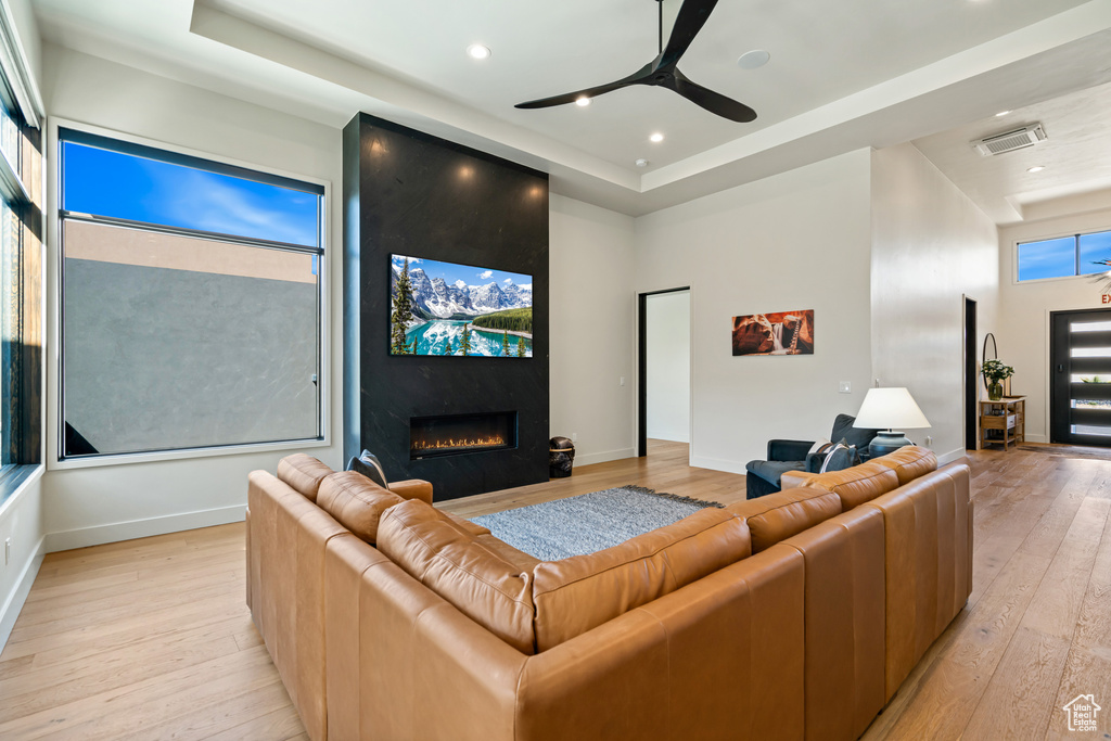 Living room with ceiling fan, a high end fireplace, and light hardwood / wood-style floors