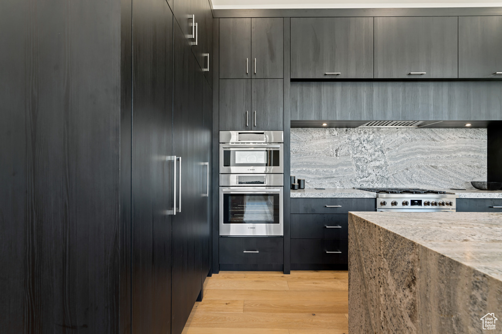 Kitchen with appliances with stainless steel finishes, light stone countertops, and light hardwood / wood-style floors