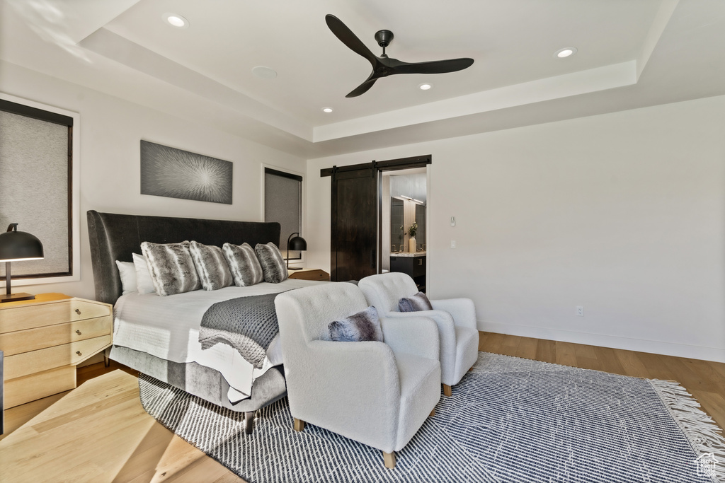 Bedroom with a barn door, ceiling fan, wood-type flooring, and a tray ceiling