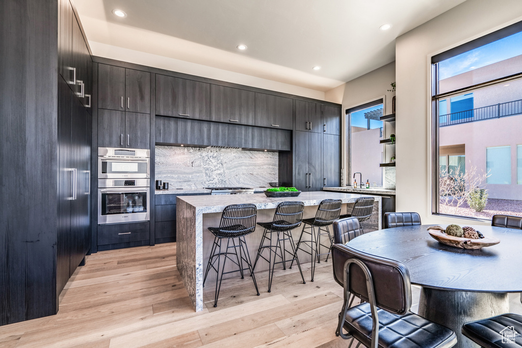 Kitchen with light hardwood / wood-style flooring, a center island, a breakfast bar, decorative backsplash, and stainless steel double oven