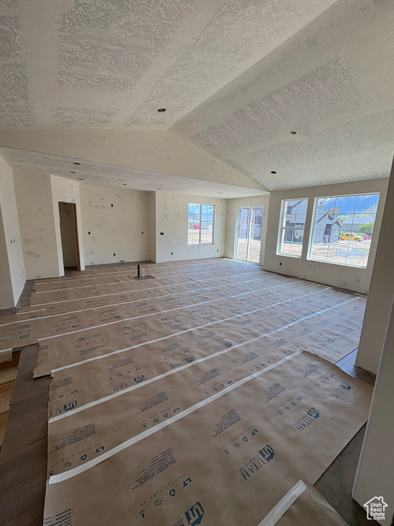 Unfurnished living room featuring vaulted ceiling and a textured ceiling