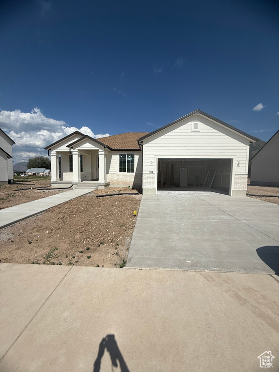 Ranch-style house featuring concrete driveway, a garage, covered porch, and brick siding