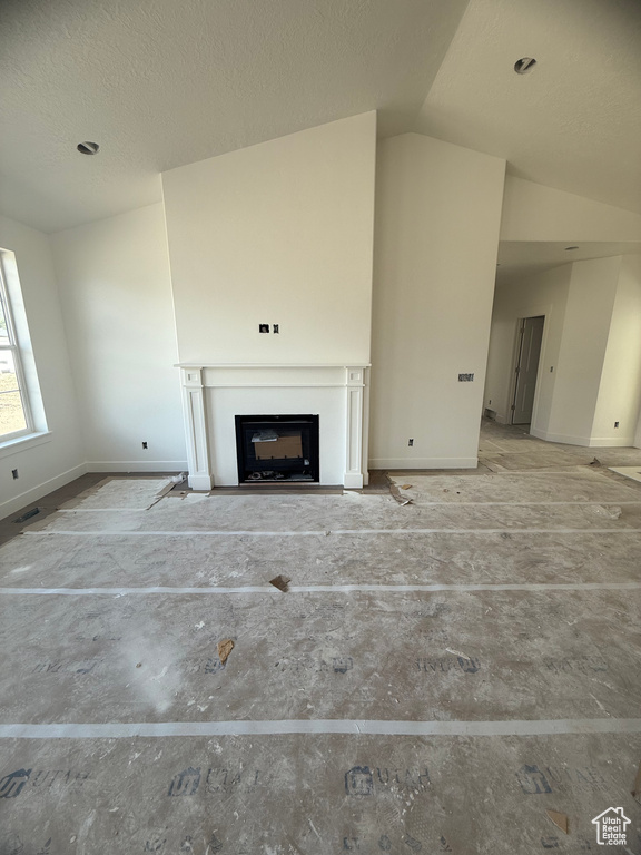 Unfurnished living room featuring baseboards, vaulted ceiling, a fireplace with flush hearth, and a textured ceiling