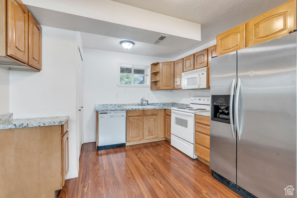 Kitchen with dark wood-type flooring, white appliances, light stone counters, and sink