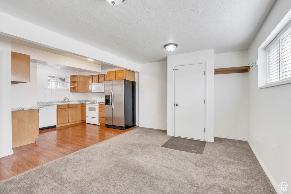 Kitchen featuring carpet flooring, white appliances, sink, light brown cabinets, and a textured ceiling