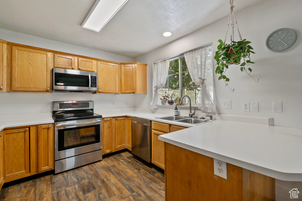 Kitchen with dark wood-type flooring, appliances with stainless steel finishes, kitchen peninsula, and sink