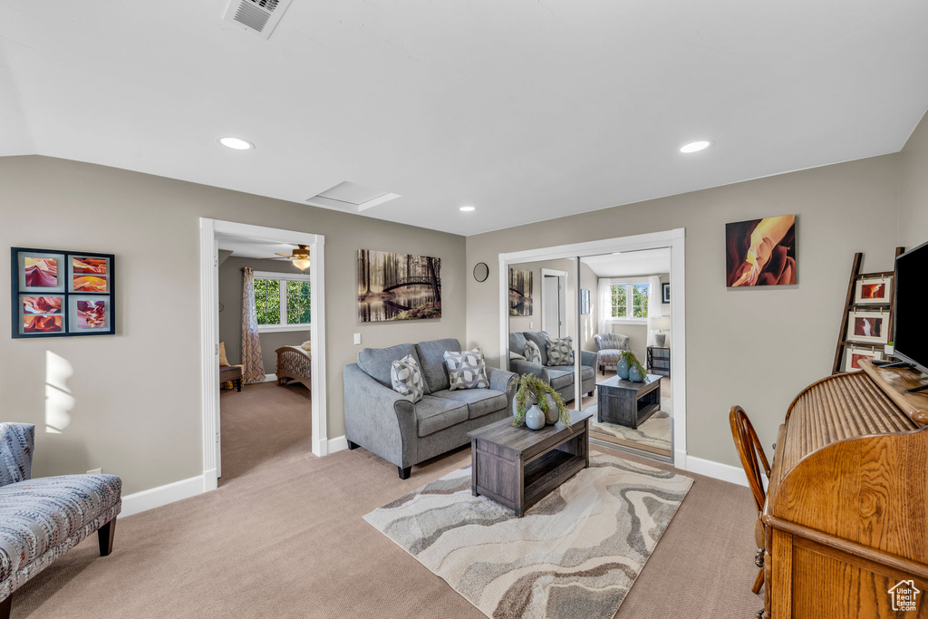 Living room with a wealth of natural light, light colored carpet, vaulted ceiling, and ceiling fan