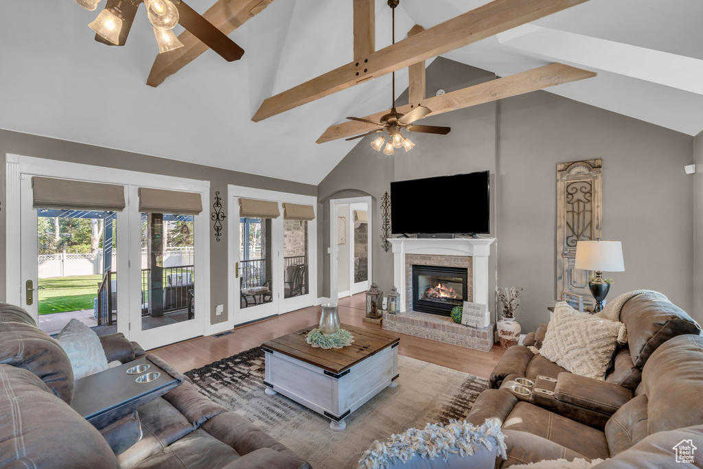 Living room with hardwood / wood-style flooring, a brick fireplace, ceiling fan, high vaulted ceiling, and beam ceiling