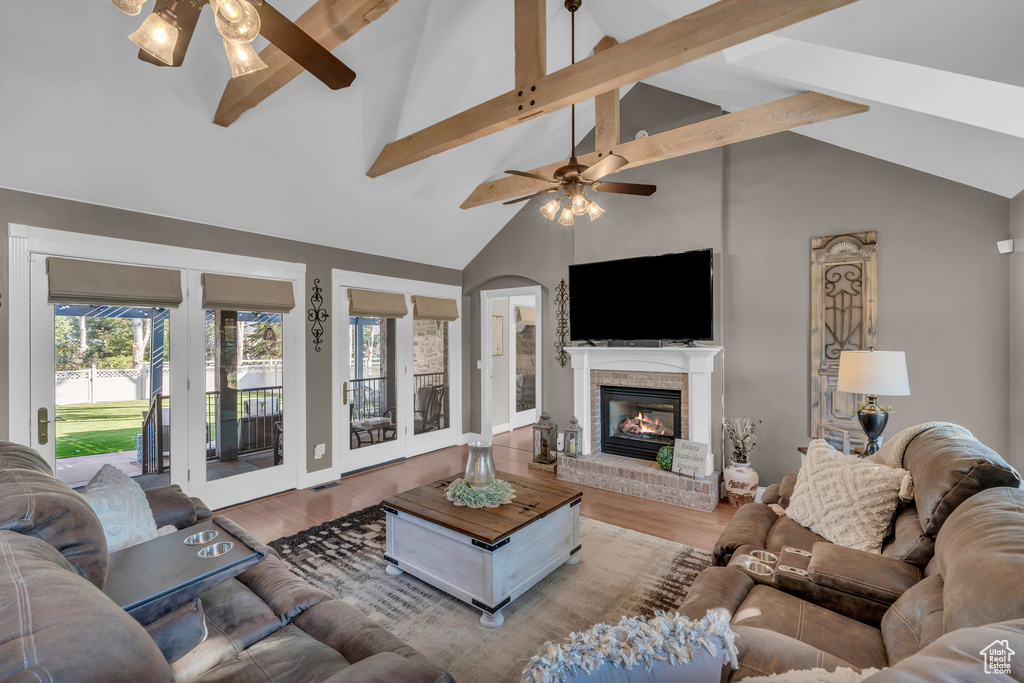 Living room featuring ceiling fan, a fireplace, wood finished floors, and beam ceiling