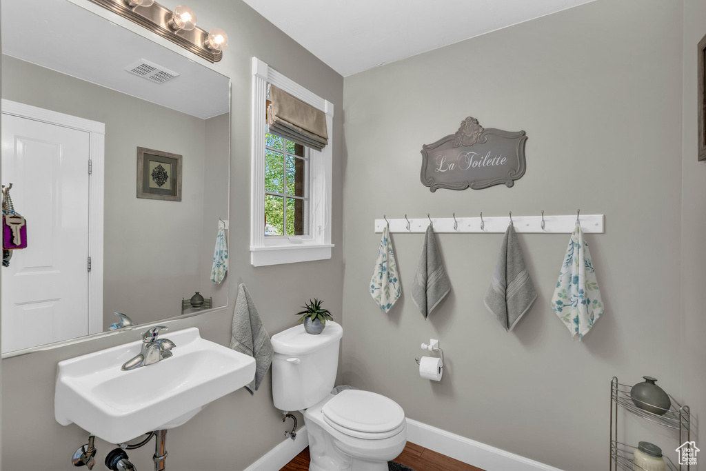 Bathroom featuring visible vents, toilet, a sink, wood finished floors, and baseboards
