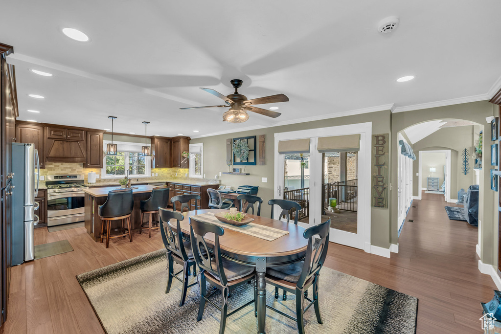 Dining space with arched walkways, baseboards, wood finished floors, and crown molding