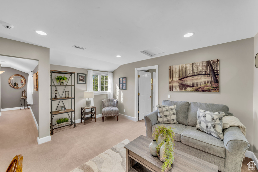 Living area with visible vents, attic access, light carpet, vaulted ceiling, and baseboards