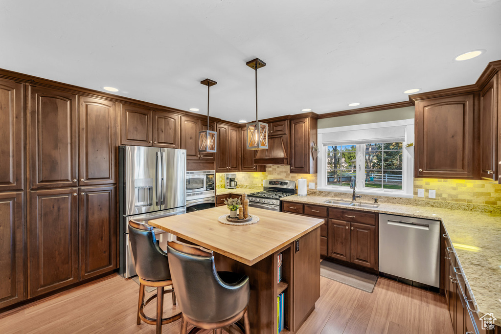 Kitchen featuring stainless steel appliances, hanging light fixtures, wooden counters, a kitchen island, and a sink