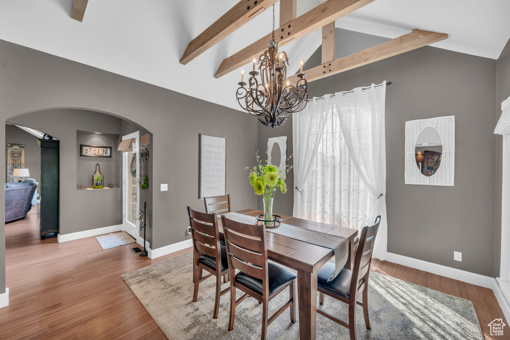 Dining room featuring arched walkways, lofted ceiling with beams, wood finished floors, and baseboards