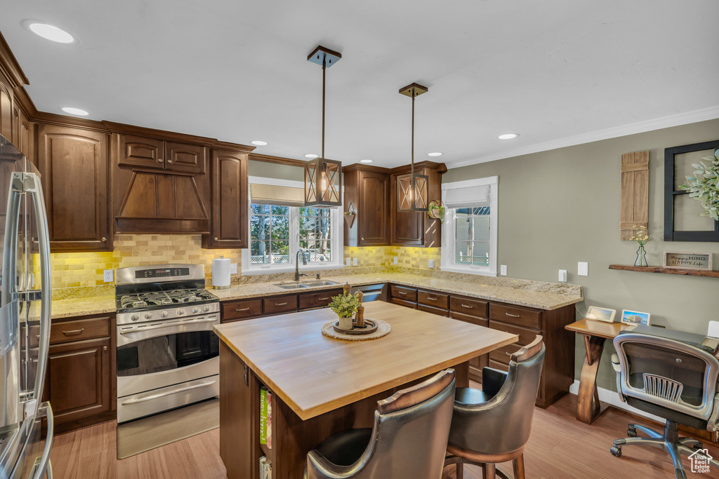 Kitchen featuring light hardwood / wood-style flooring, appliances with stainless steel finishes, butcher block countertops, pendant lighting, and a kitchen island