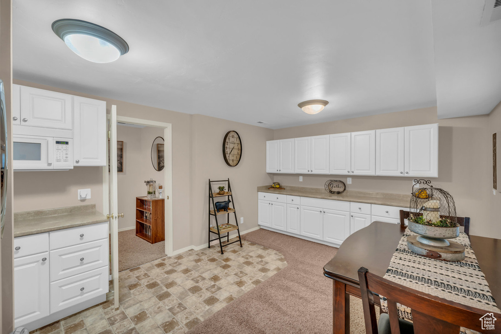 Kitchen featuring light colored carpet and white cabinets