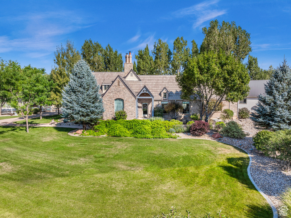 English style home featuring stone siding, a chimney, and a front lawn