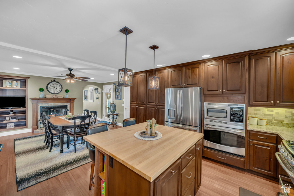 Kitchen featuring a glass covered fireplace, appliances with stainless steel finishes, open floor plan, light stone countertops, and pendant lighting