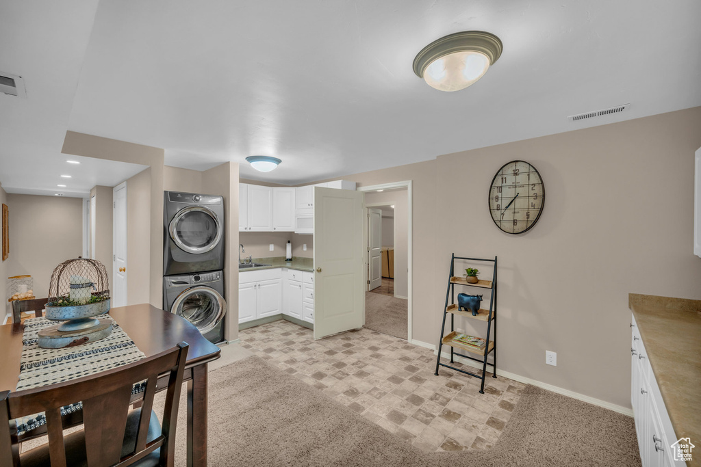 Kitchen featuring light carpet, stacked washing maching and dryer, white cabinetry, and sink