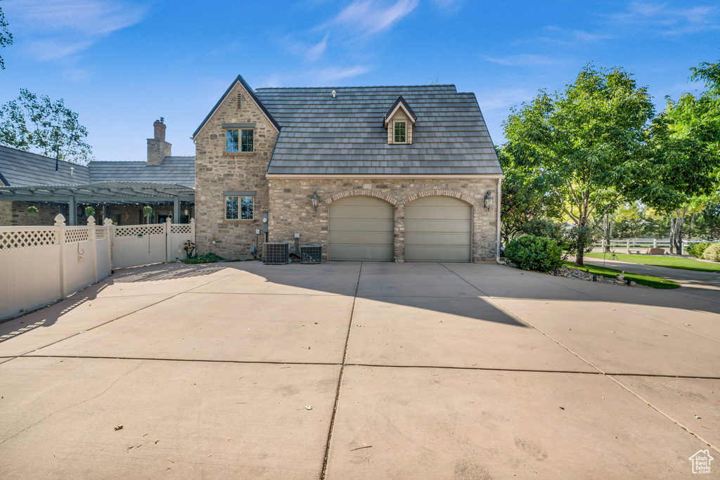 View of front facade with central air condition unit, an attached garage, fence, stone siding, and driveway