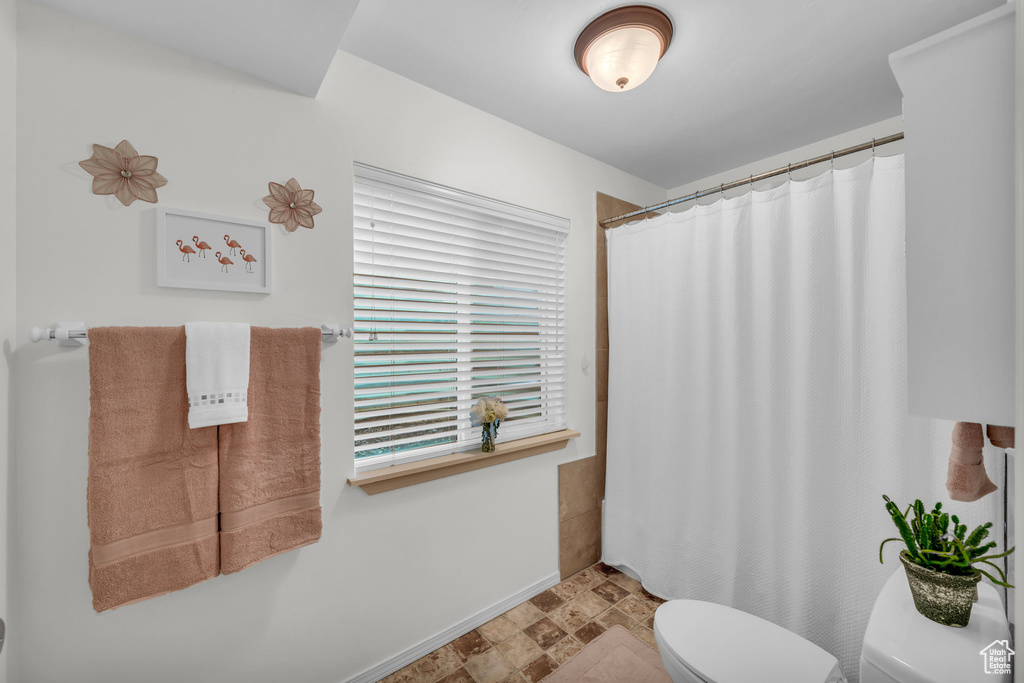 Bathroom featuring a shower with shower curtain, toilet, and a healthy amount of sunlight