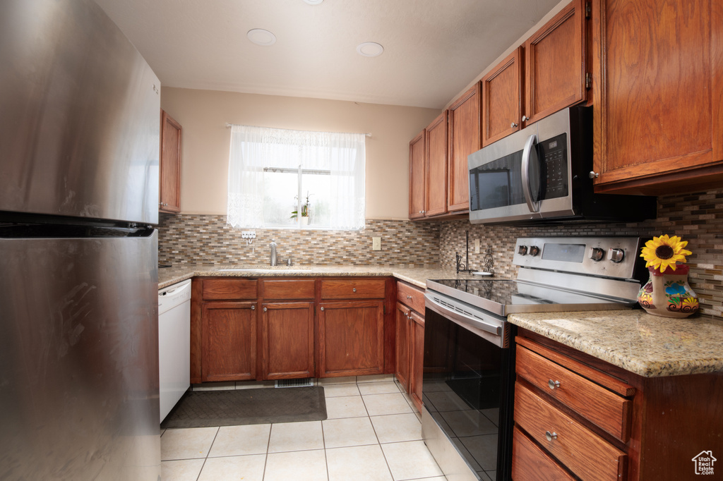 Kitchen with light stone counters, appliances with stainless steel finishes, light tile patterned floors, and backsplash