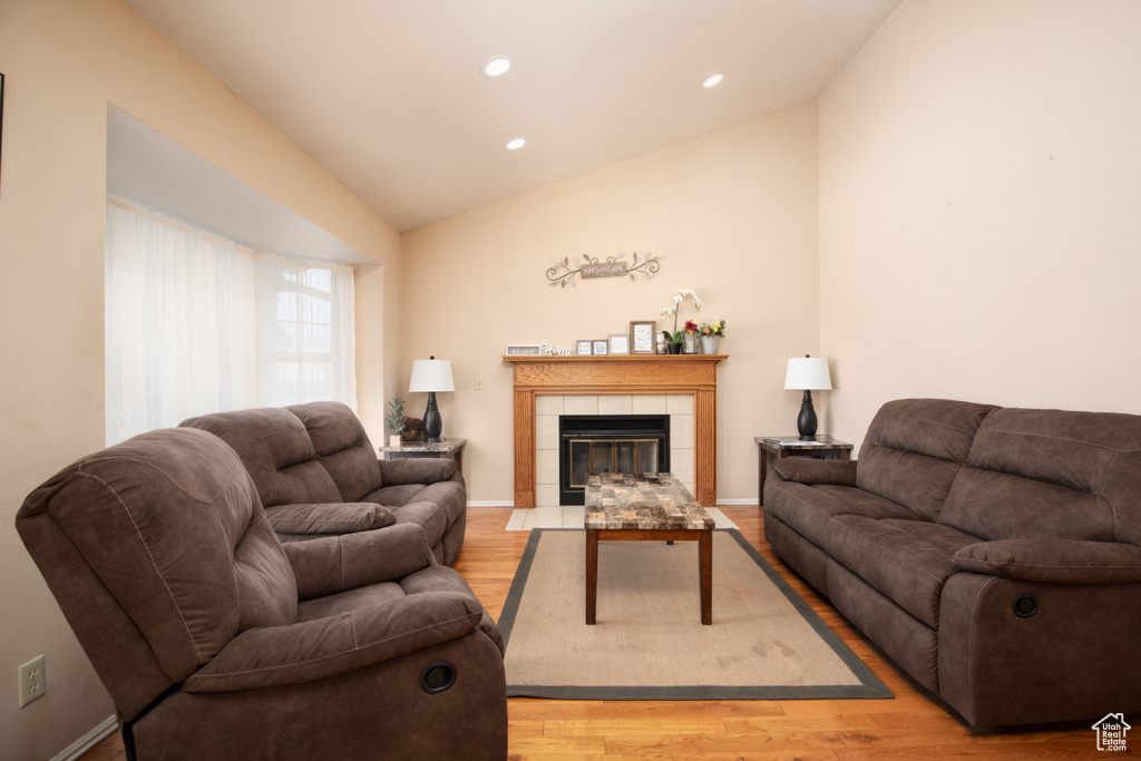 Living room featuring a tiled fireplace, lofted ceiling, and light hardwood / wood-style flooring