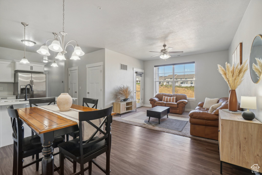 Dining space featuring ceiling fan with notable chandelier, a textured ceiling, and dark hardwood / wood-style floors