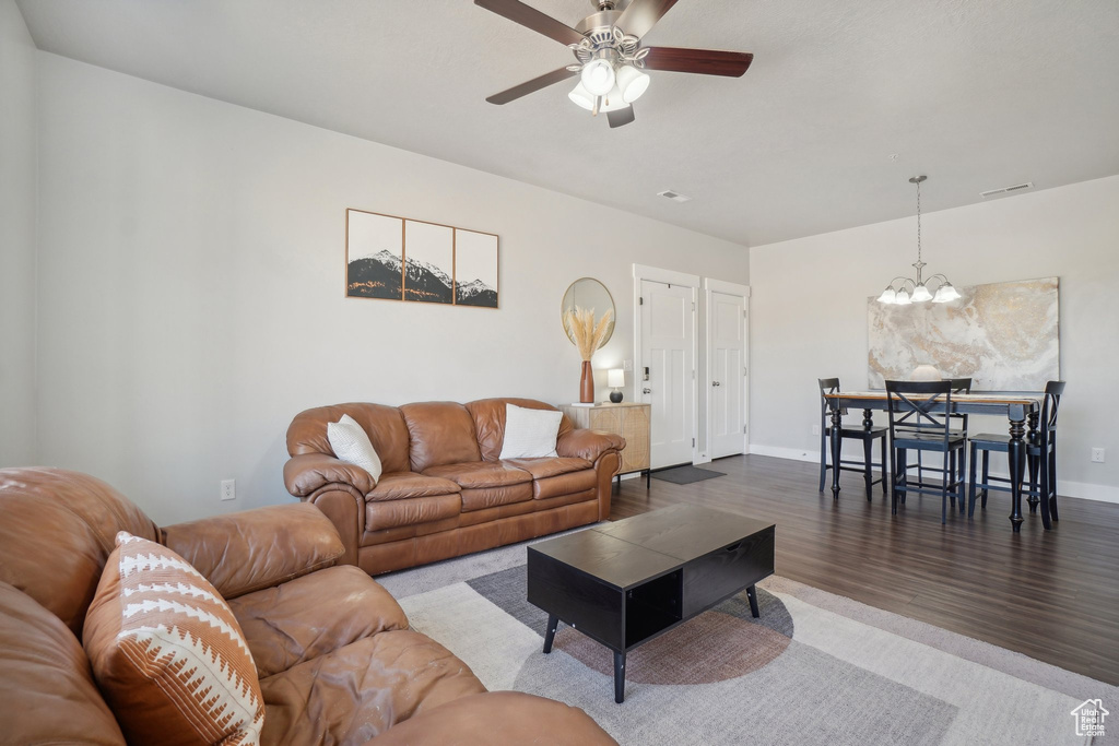 Living room with ceiling fan with notable chandelier and wood-type flooring