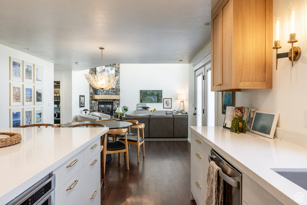 Kitchen with dishwasher, a stone fireplace, dark wood-type flooring, a chandelier, and white cabinets