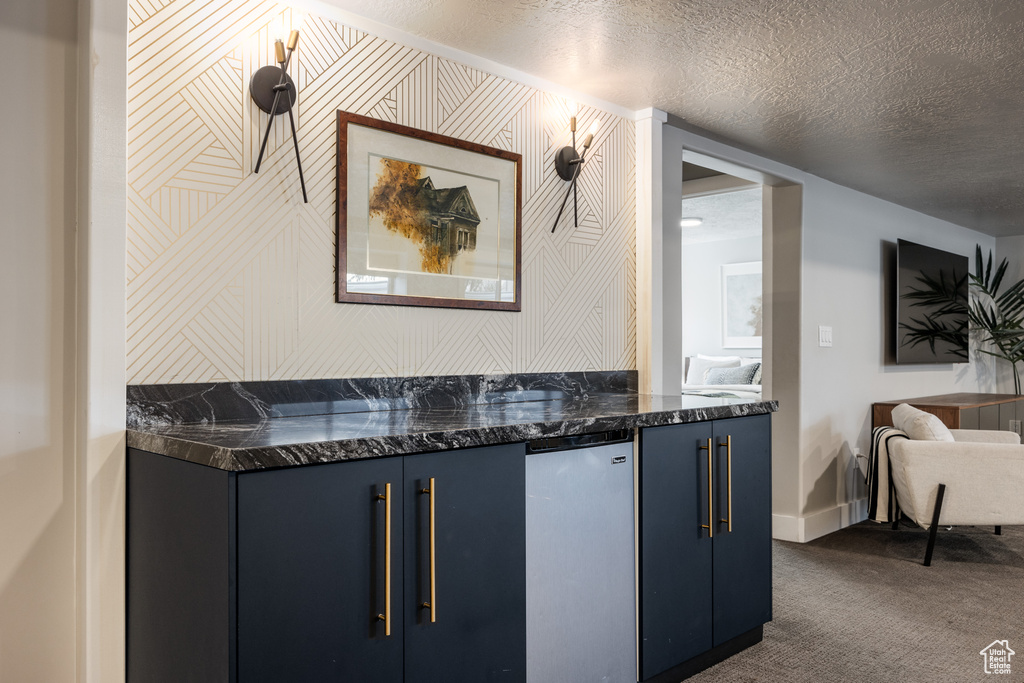 Bar with dark carpet, dark stone countertops, a textured ceiling, and blue cabinetry