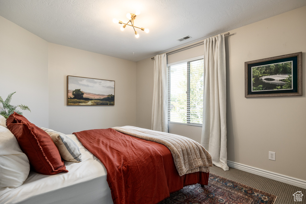 Carpeted bedroom featuring a textured ceiling and an inviting chandelier