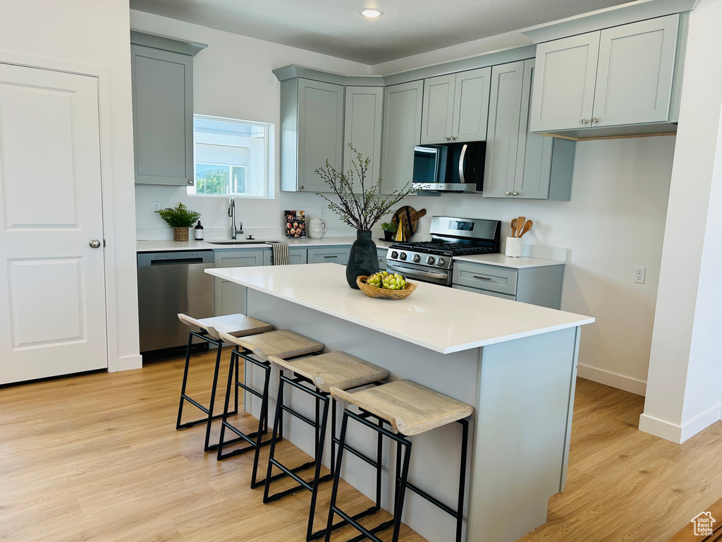 Kitchen with appliances with stainless steel finishes, sink, a kitchen breakfast bar, and light hardwood / wood-style flooring