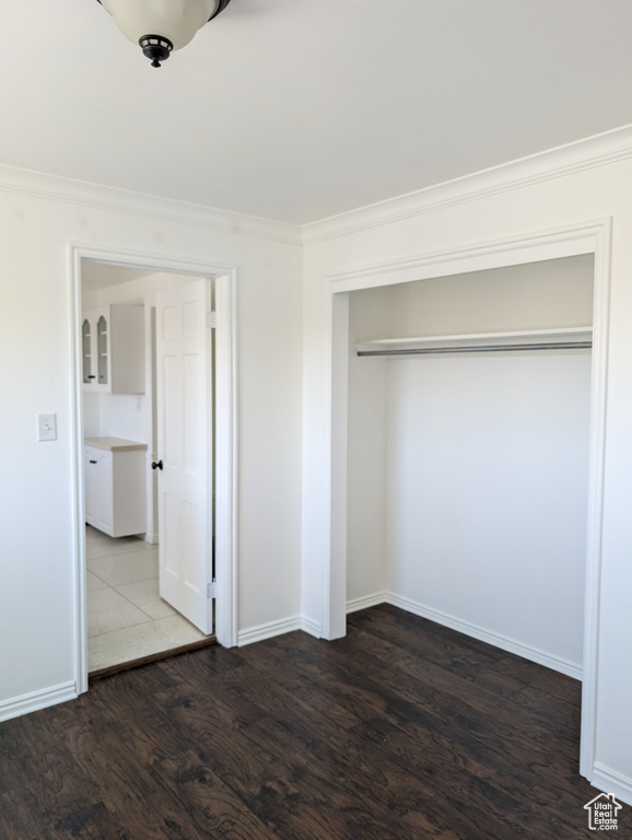 Unfurnished bedroom featuring a closet, ornamental molding, and dark hardwood / wood-style floors