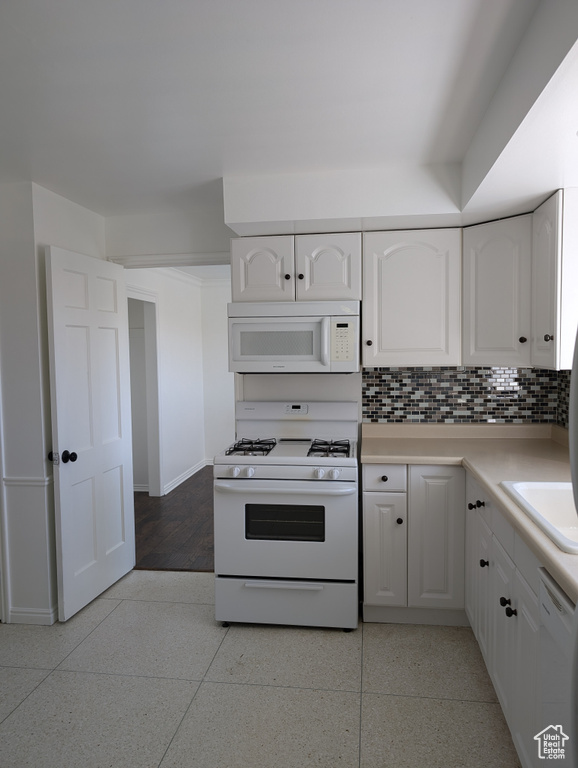 Kitchen featuring sink, decorative backsplash, white cabinets, and white appliances