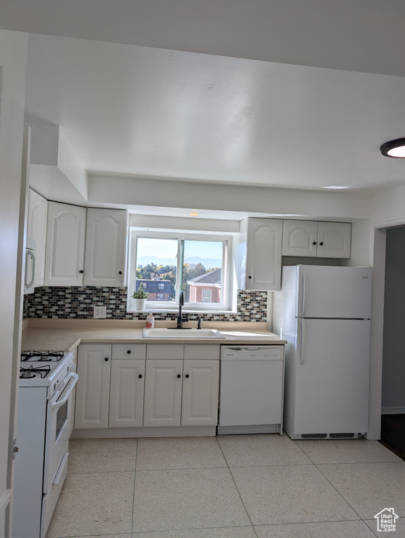 Kitchen with white appliances, backsplash, white cabinetry, and sink