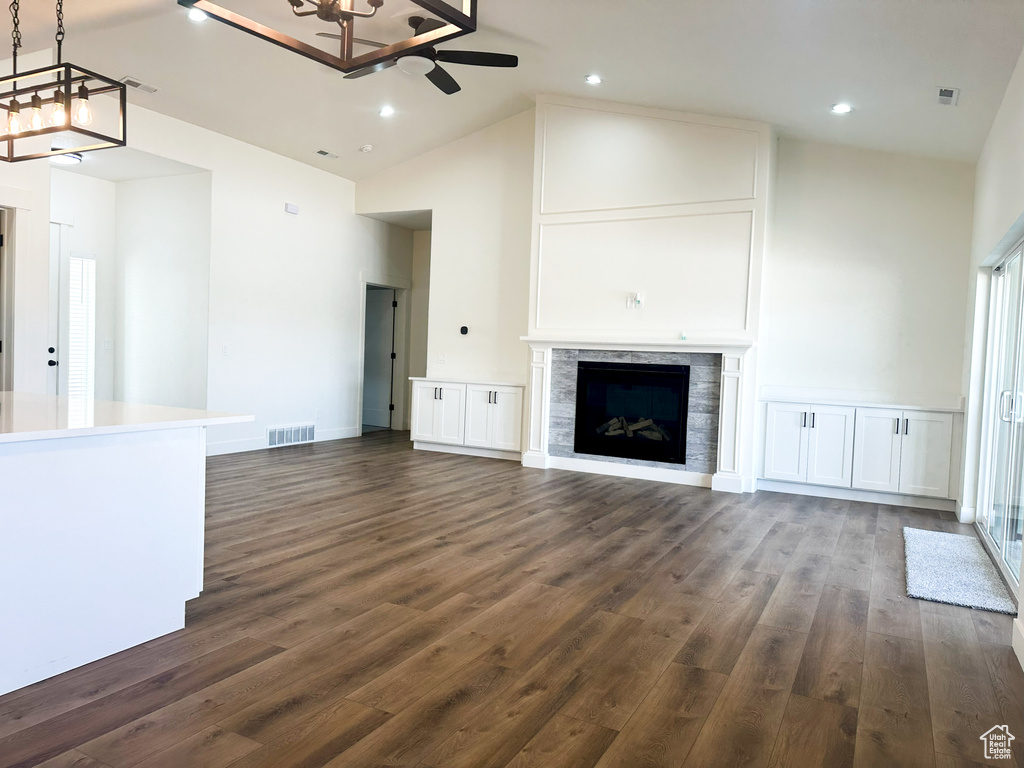 Unfurnished living room with ceiling fan with notable chandelier, high vaulted ceiling, and dark hardwood / wood-style flooring