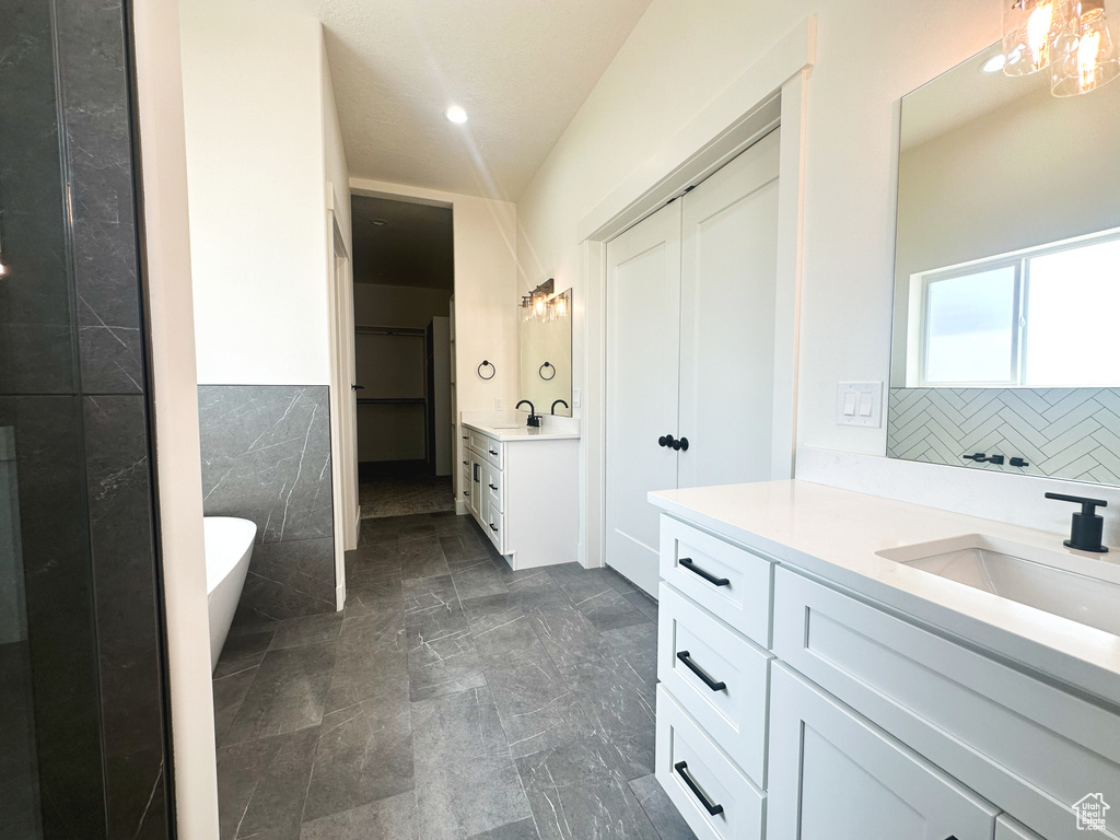 Bathroom featuring vanity, a bathing tub, tile walls, and a chandelier