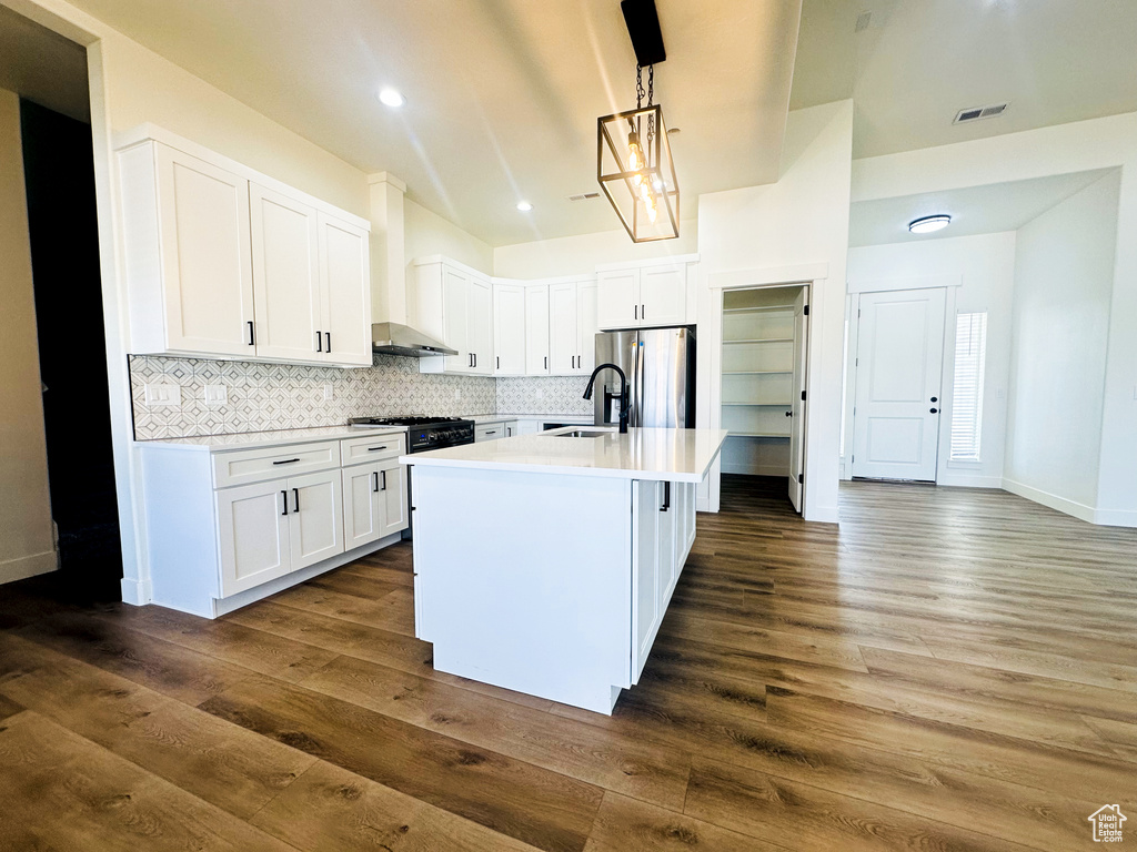 Kitchen with white cabinetry, dark hardwood / wood-style flooring, stainless steel appliances, and an island with sink