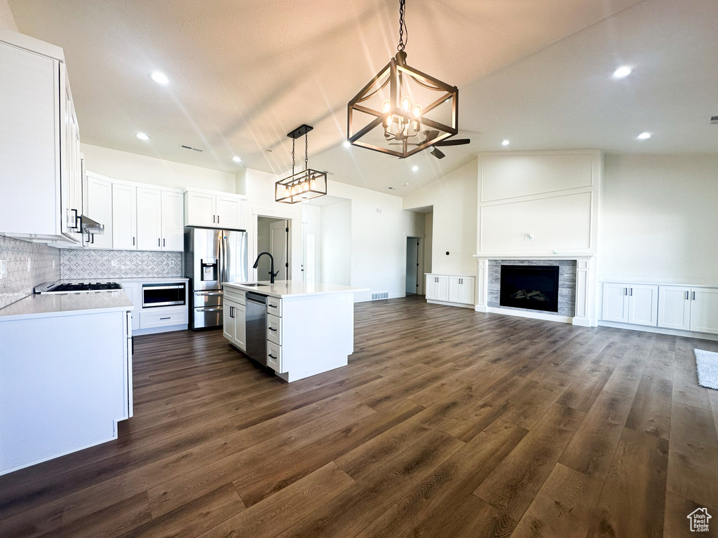 Kitchen with a notable chandelier, an island with sink, hanging light fixtures, appliances with stainless steel finishes, and lofted ceiling