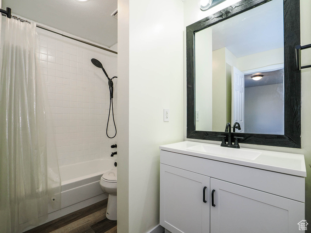 Full bathroom with hardwood / wood-style floors, toilet, shower / tub combo, and vanity