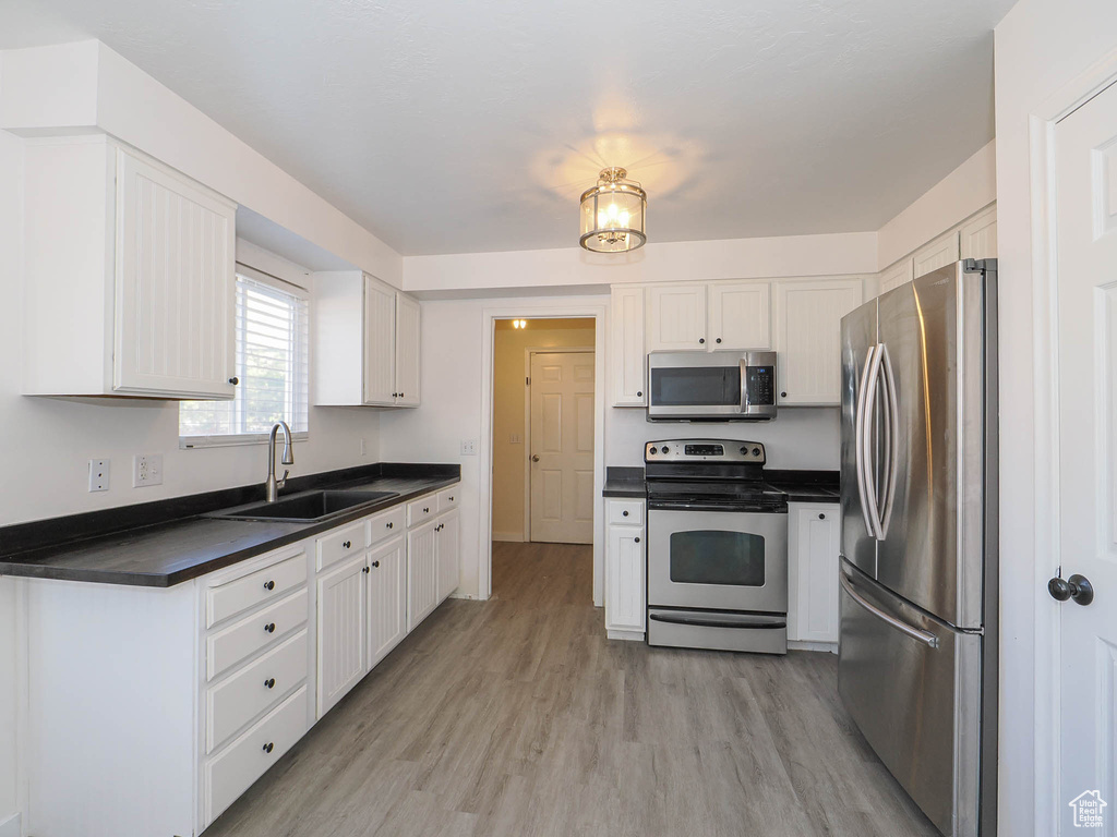 Kitchen with sink, appliances with stainless steel finishes, white cabinets, and light hardwood / wood-style floors