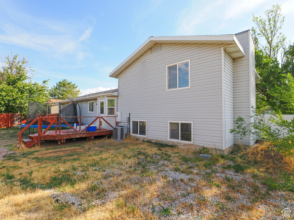 Back of property featuring central air condition unit, a wooden deck, and a yard