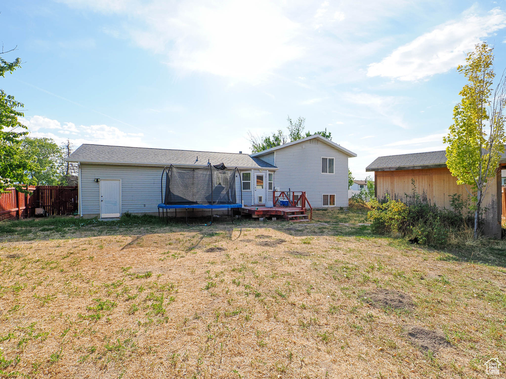 Rear view of house featuring a wooden deck, a lawn, and a trampoline