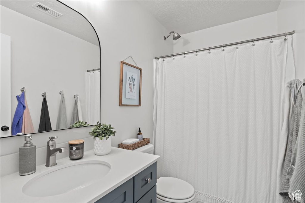 Bathroom featuring vanity, toilet, walk in shower, and a textured ceiling