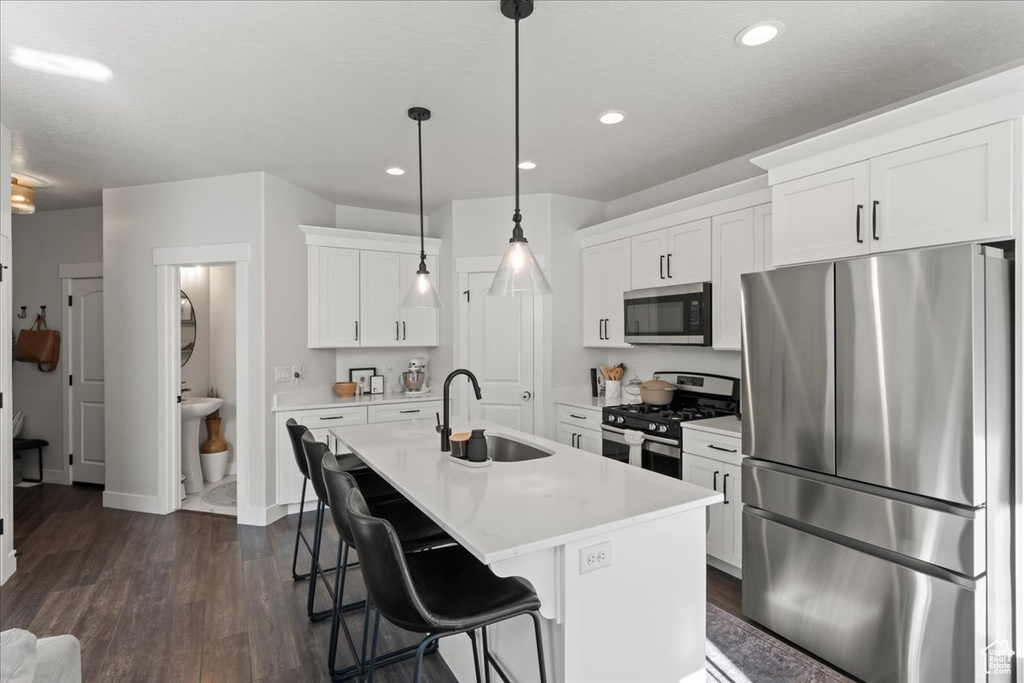 Kitchen featuring a kitchen island with sink, white cabinetry, decorative light fixtures, stainless steel appliances, and sink