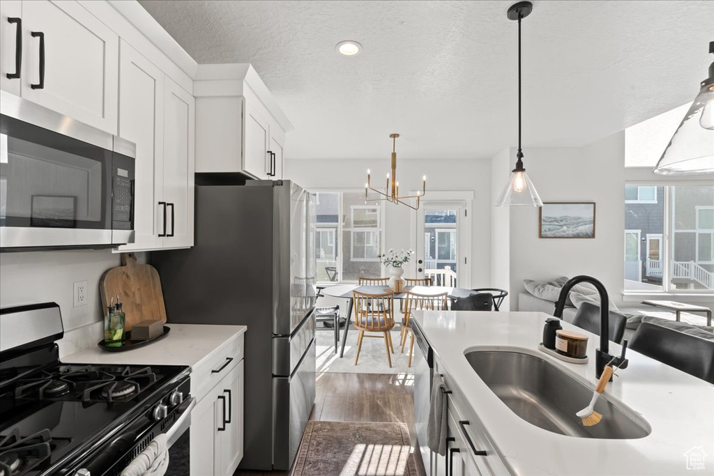 Kitchen featuring hanging light fixtures, appliances with stainless steel finishes, dark hardwood / wood-style flooring, white cabinetry, and sink