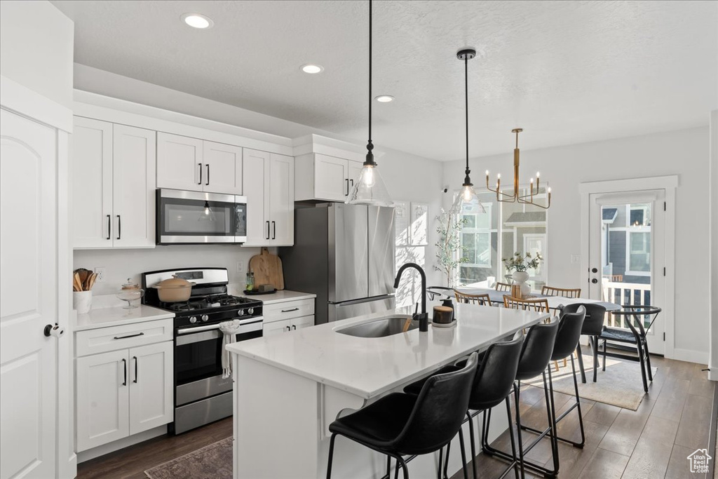 Kitchen featuring a kitchen island with sink, white cabinetry, stainless steel appliances, sink, and dark hardwood / wood-style floors