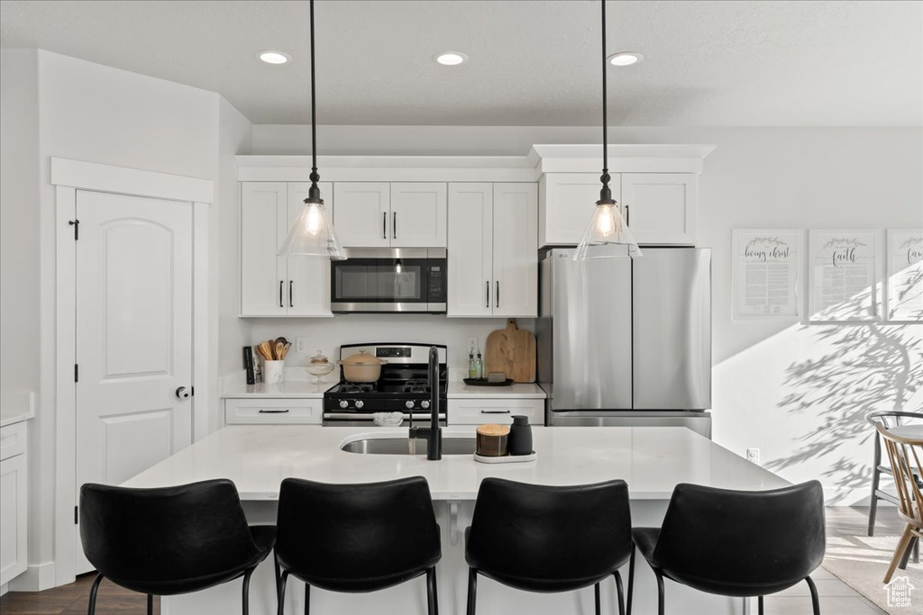 Kitchen featuring white cabinetry, wood-type flooring, a breakfast bar, appliances with stainless steel finishes, and a center island with sink