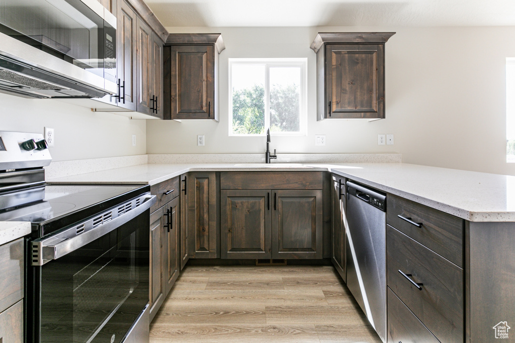 Kitchen featuring sink, kitchen peninsula, dark brown cabinets, light hardwood / wood-style flooring, and appliances with stainless steel finishes